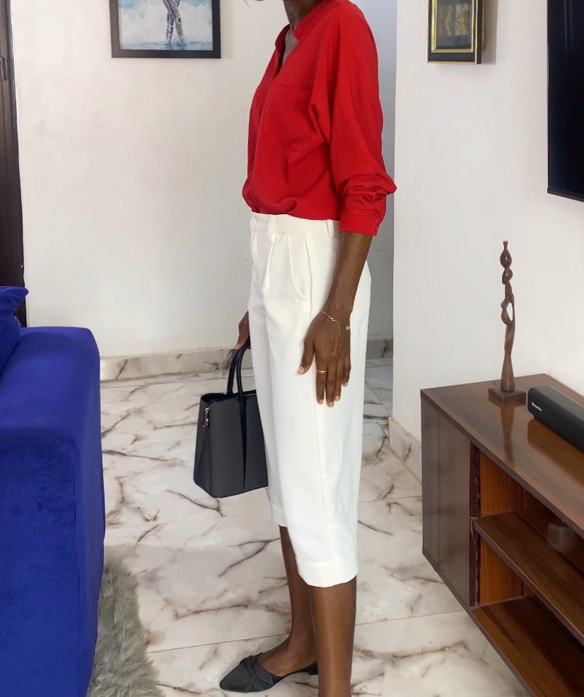 Woman in a red top and white skirt standing in a living room. Women's tailored jorts. Business casual shorts for women, Knee-length women's shorts, Tailored women's shorts